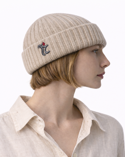 Person wearing a beige knit beanie with a logo on a white background 